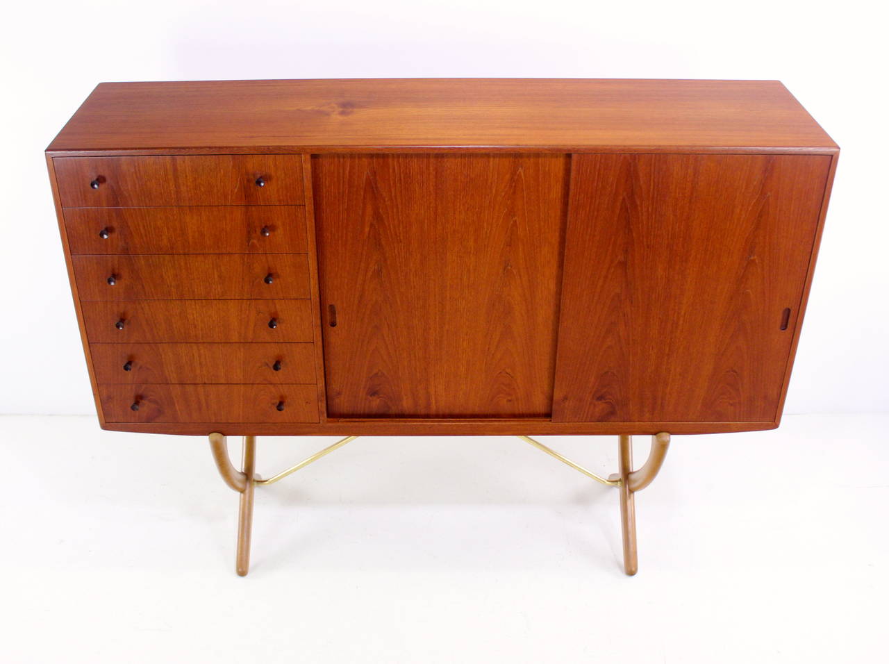 Danish modern cabinet designed by Hans Wegner in 1951.
Carl Hansen & Sons, maker. Model CH304.
Teak cabinet with oak interior.
Extraordinary oak and solid brass saber legs.
Six pull-out trays on left.
Doors slide open to adjustable shelving in