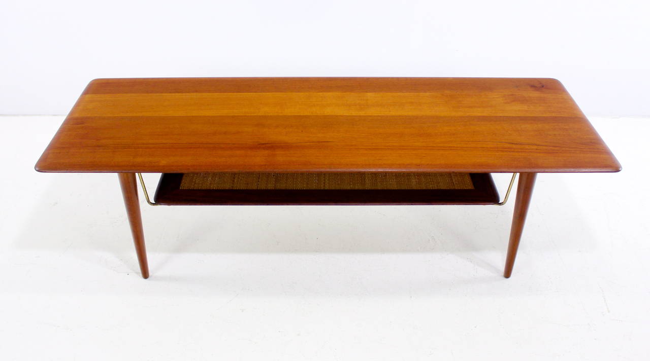 Danish modern coffee table designed by Peter Hvidt.
Richly grained teak.
Lower magazine shelf of teak and cane secured with brass hardware.
A Peter Hvidt Classic.
Professionally restored and refinished by LookModern.
Matchless quality and