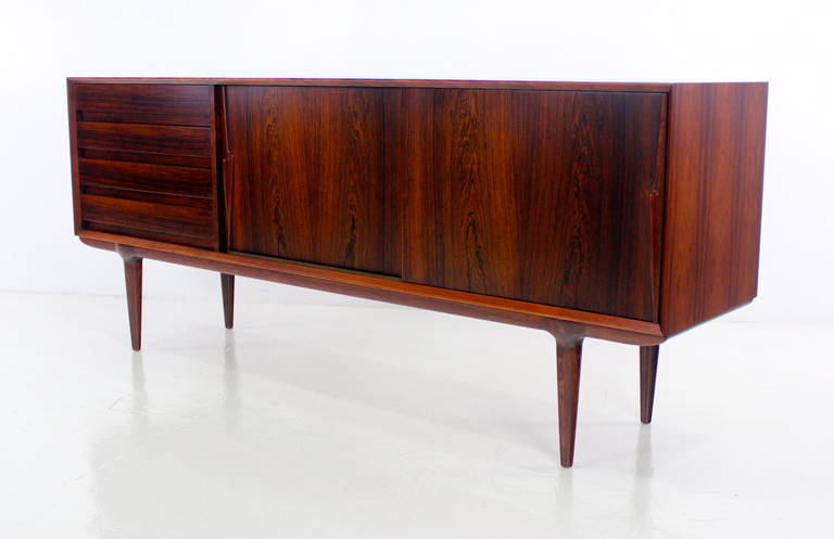 Danish modern credenza designed by Omann Jun. Model #18.
Extraordinary flame grained rosewood with inset drawer pulls and sensuously styled door handles.
Sliding doors open to adjustable shelf in center and right.
Four drawers on the