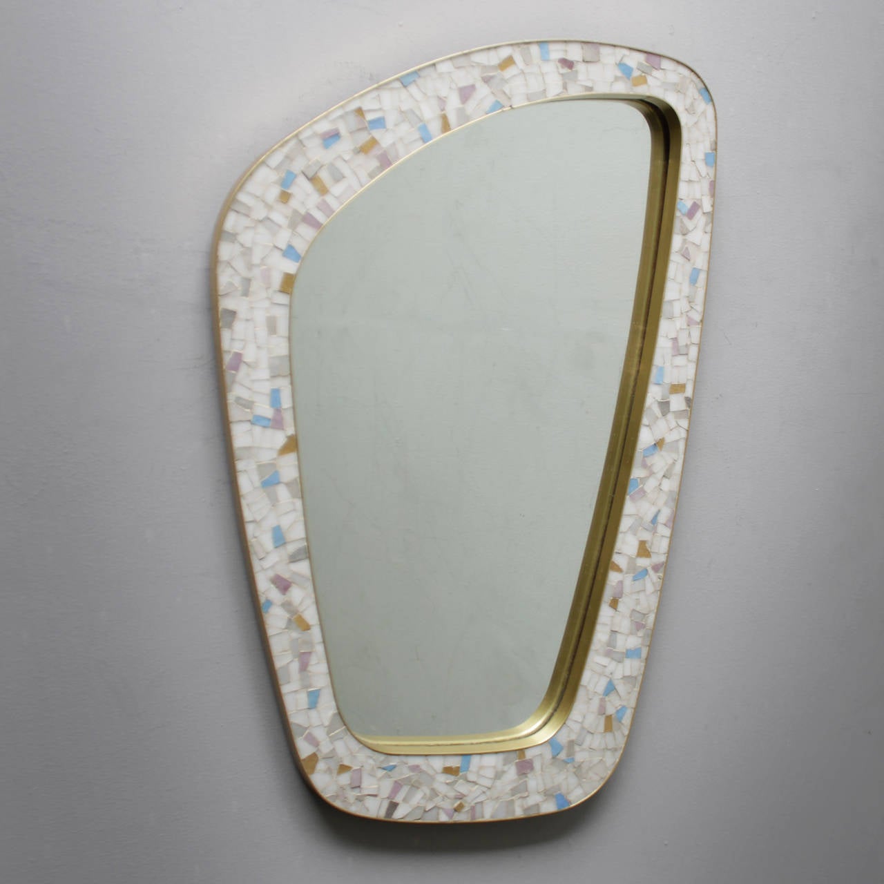 Striking mirror executed in a typical Free-Form, asymmetrical shape. 
Materials:	mosaic tiles, brass and mirror glass.
Though the origins of this piece are unknown, the craftsmanship and the brass trimmings indicate that the mirror is most likely