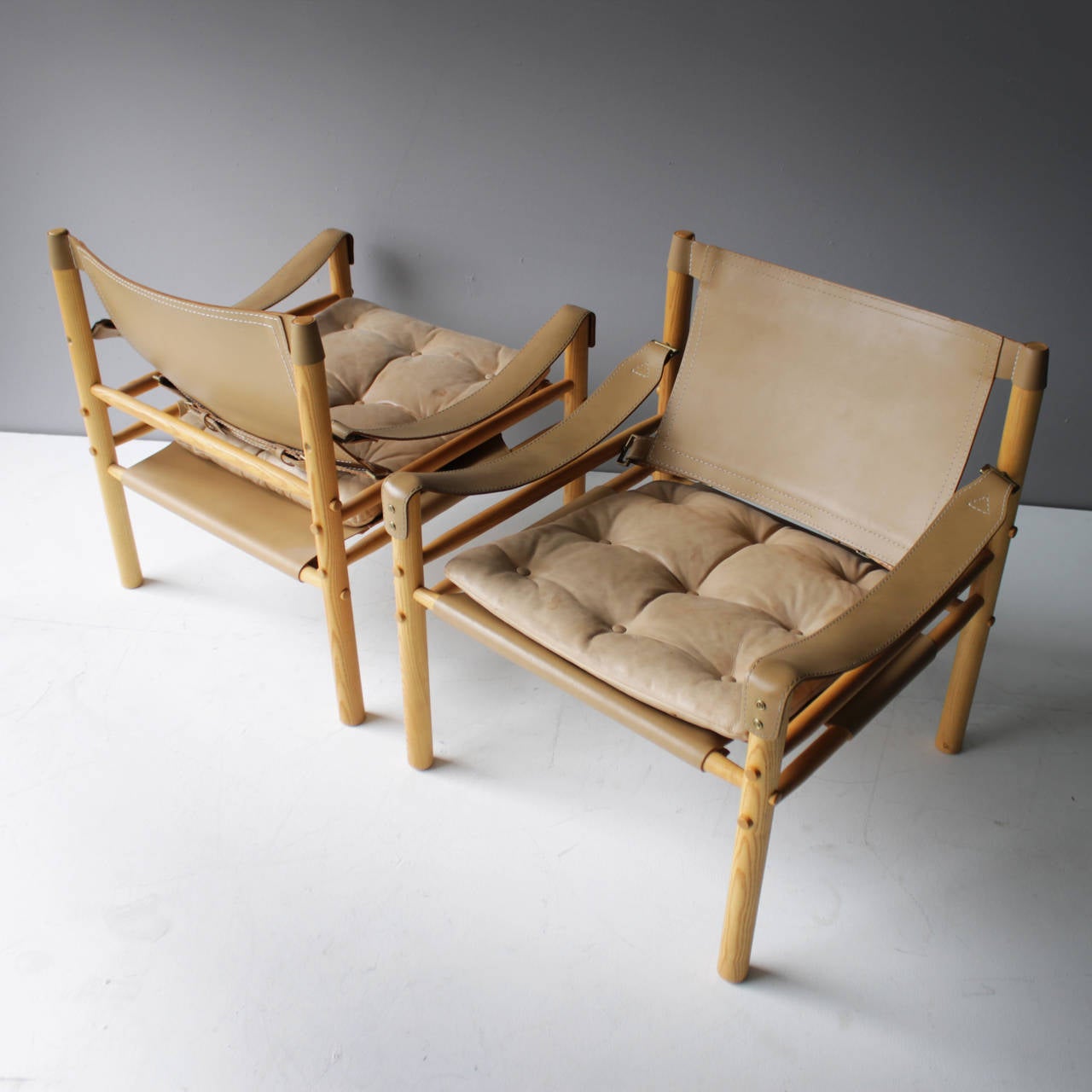 A pair of 'Scirocco' safari chairs by Arne Norell with varnished ash frame mounted with pale sandy harness leather, loose seat cushions with buttoned leather covers. 
Produced by Aneby Møbler.