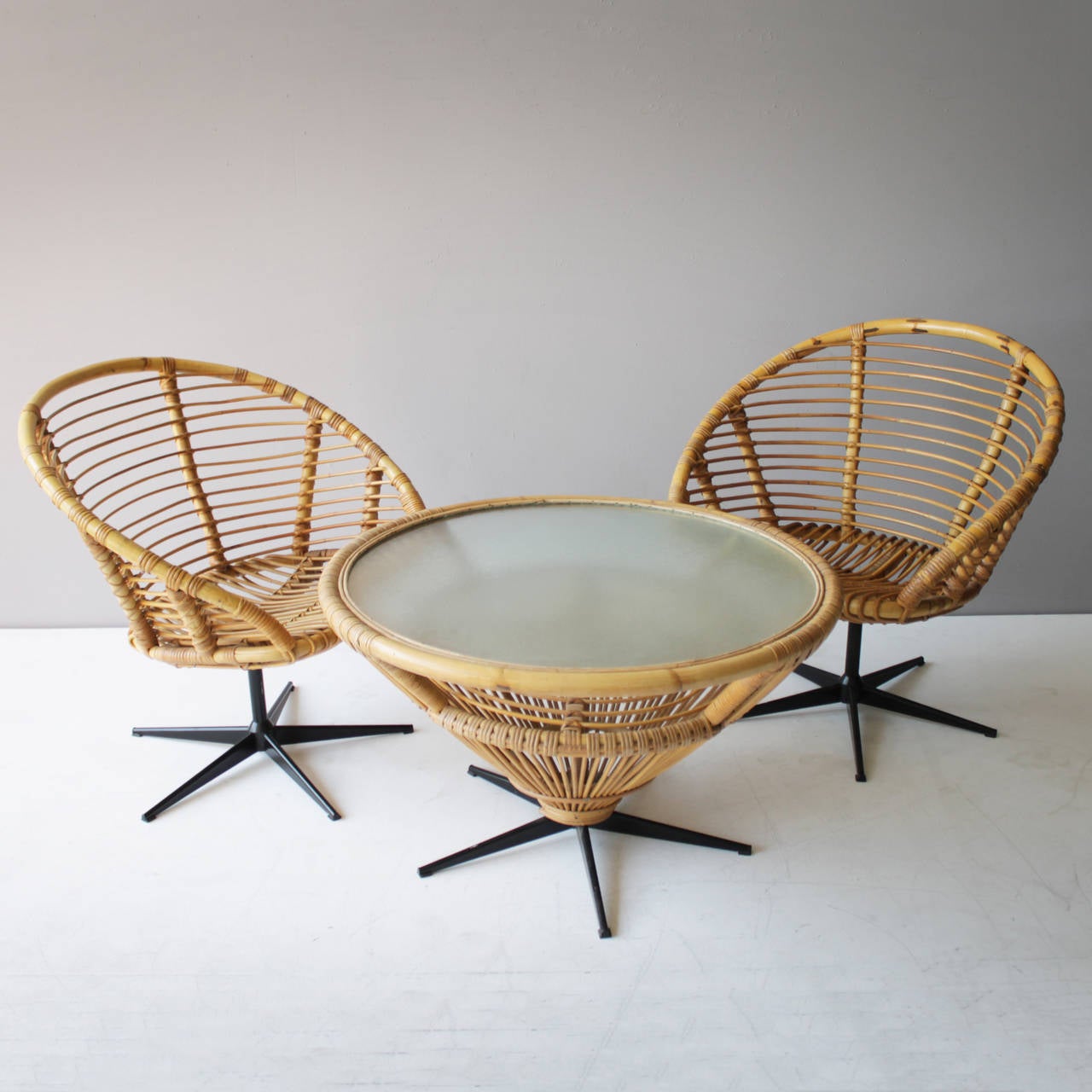 Set of four rattan swivel chairs in the style of Franco Albini. Rattan with cane chairs with cushions on a black lacquered metal star base. Beautiful condition. We also offer the matching table (see picture).