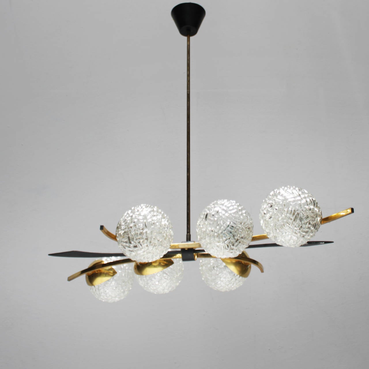 Pendant light of the 1950s in the style of Stilnovo. Construction of brass, gold colored metal and black metal, six burners, each with a diffuser made ​​of clear, structured glass. Diameter sphere: 5.5 inches (14 cm).