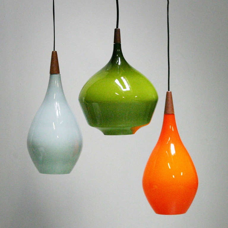 Set of three Danish pendant lights by Holmegaard Kastrup. Marked with 'Made in Denmark'. Teak and glass. 
In the colors deep orange, light blue and green. Diameter: 7.4 in. (19 cm) orange and light blue lamp; 8.6 in. (22 cm) green lamp. Height: