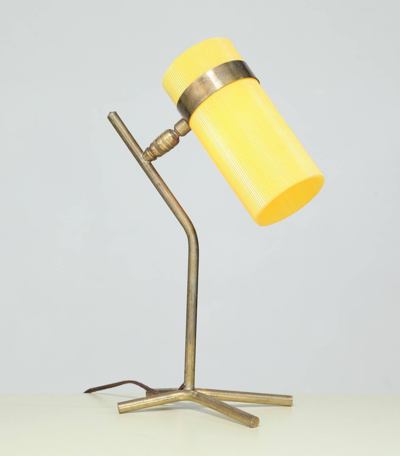 A petite French table lamp reminiscent of the work of Boris Lacroix and Pierre Guariche, made of a yellow plastic cylinder shade on brass feet. The ball construction allows the shade to be turned in any direction.