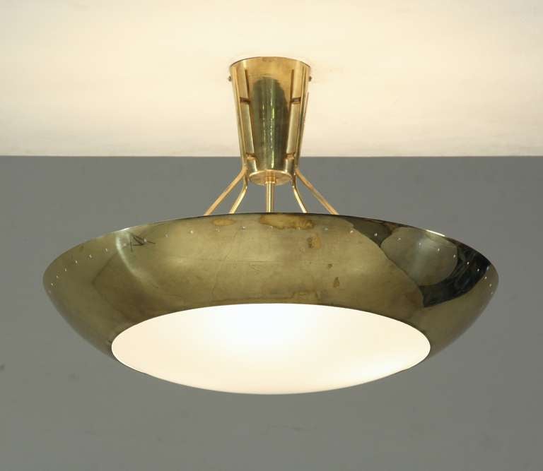 A large, round ceiling lamp from Finland, made of brass and a milky white convex plexiglass diffuser and three light bulbs. The shade has small round perforations around the edge, for a beautiful light distribution. It hangs from four brass rods,