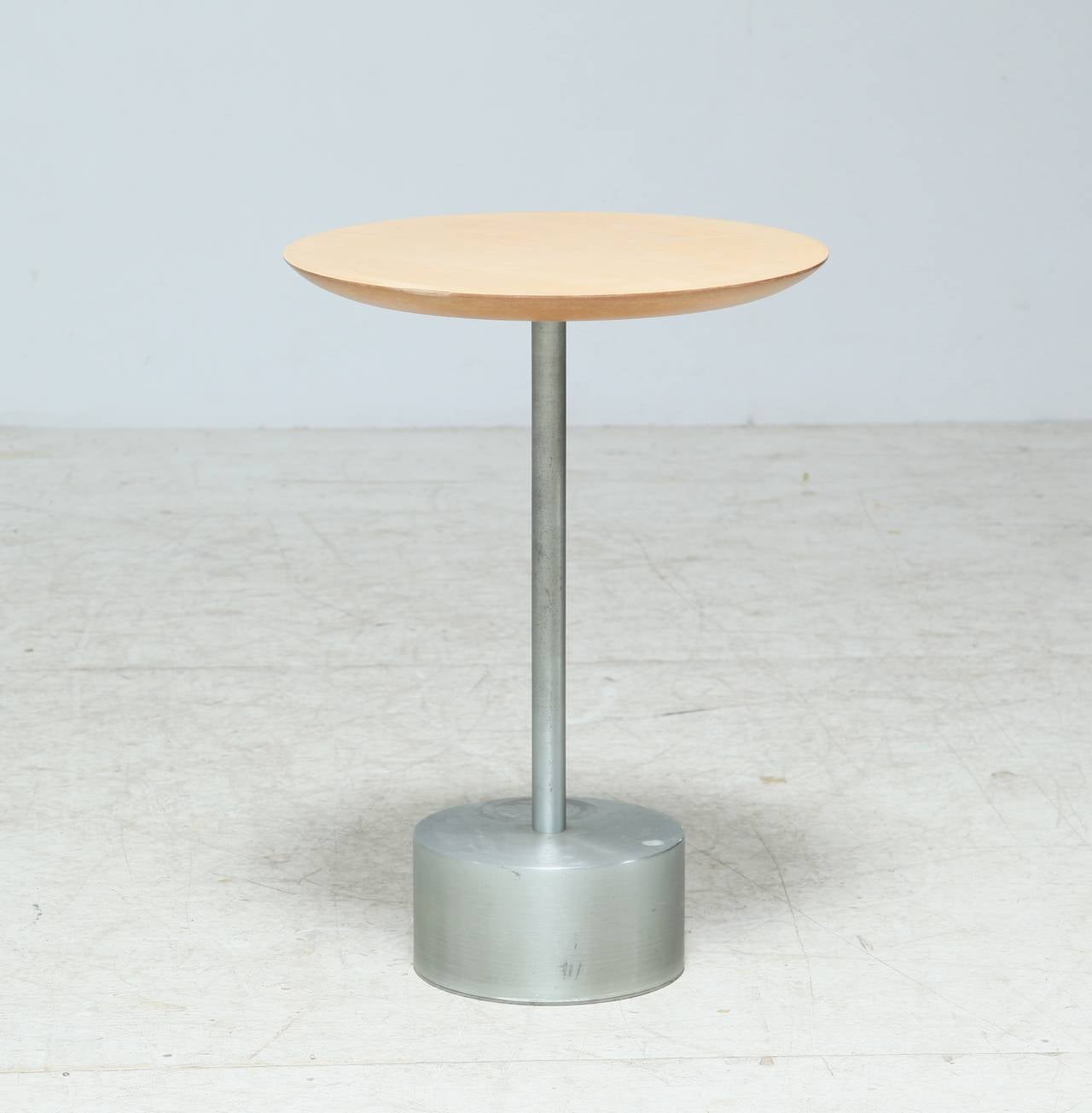 A round birch side table on an aluminum base.