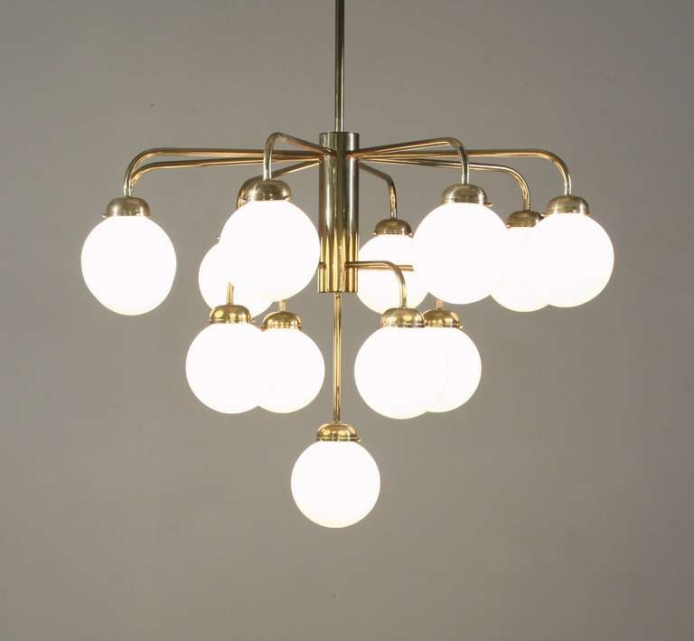 Un grand lustre allemand en laiton des années 1960. Ce lustre est fixé au plafond par une longue tige et comporte 13 bras sur trois niveaux différents. Chaque bras porte un abat-jour en forme de globe opalin. 

La chute totale peut être ajustée.