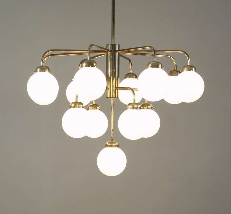 A large German brass chandelier from the 1960s. This chandelier is attached to the ceiling with a long stem and has 13 arms on three different levels. Each arm holds an opaline globe shade. 

Total drop can be adjusted.