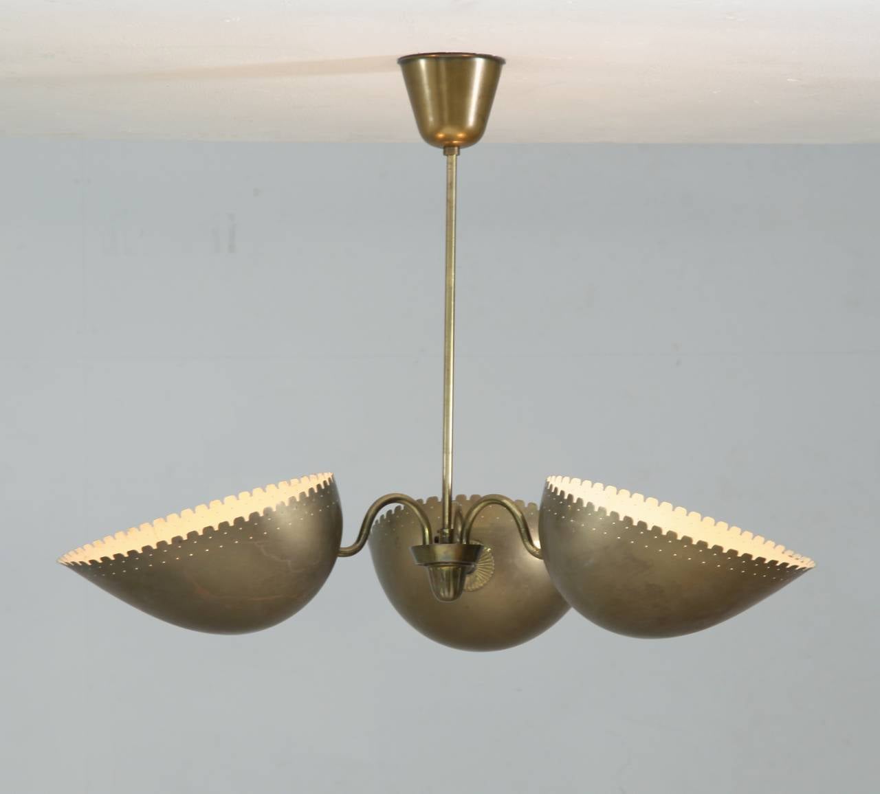 A brass pendant from Sweden, attributed to Bertil Brisborg for Bohlmarks. The lamp has, three shades with serrated and perforated edges, facing upwards.