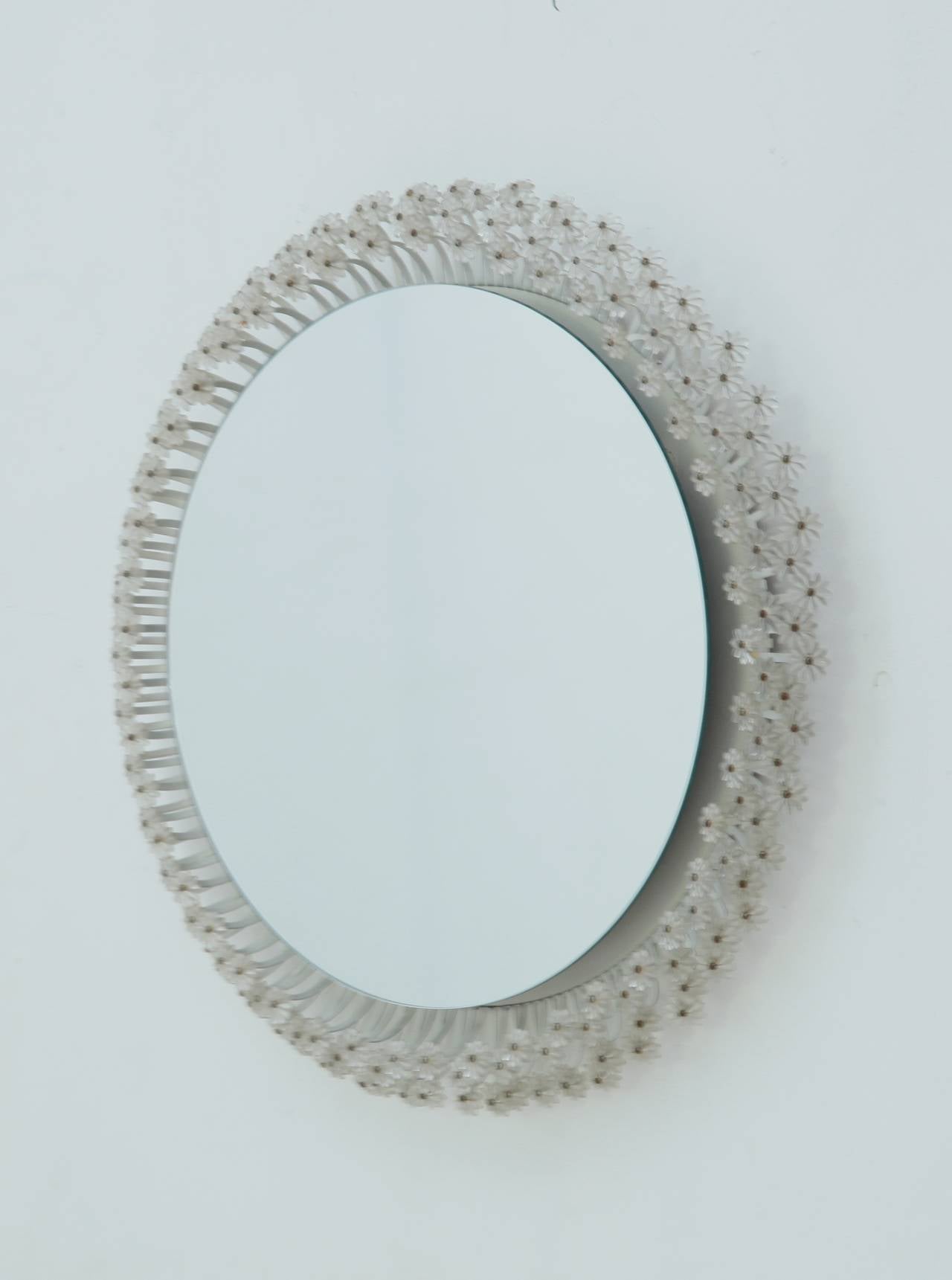 A round wall mirror with a circular tube light behind it. The mirror is surrounded with daisy-like ornaments, made of lacquered steel and plexiglass.
This mirror was designed for a cafe in Vienna in 1955.