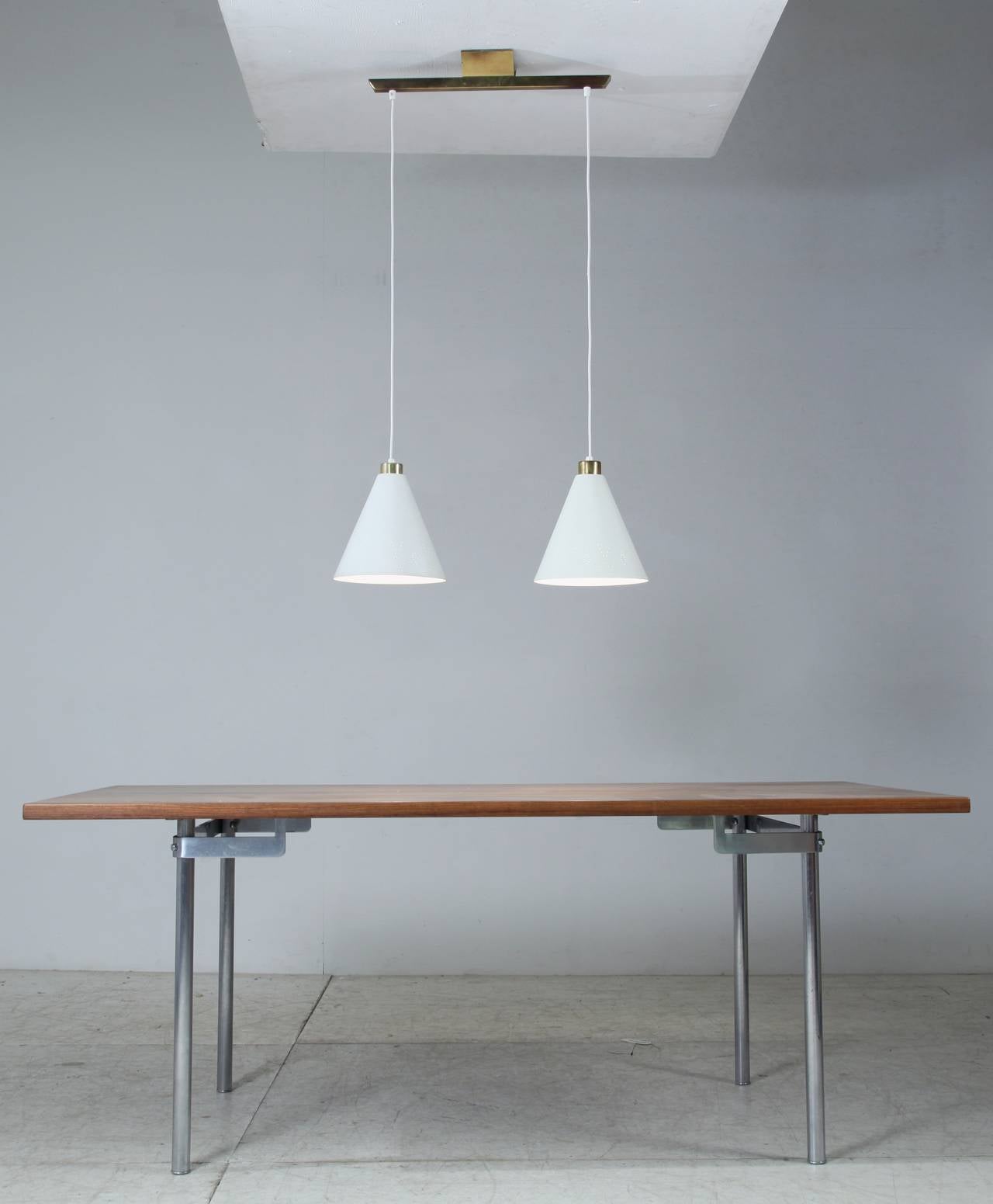A rare model K2-60 pendant by Paavo Tynell with two shades hanging from a rail. The metal shades are painted white and have the typical Tynell pinhole perforations, here in a less typical geometric pattern.