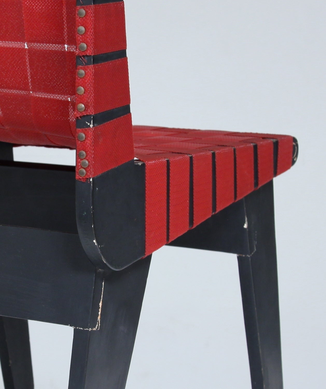 A black wooden chair with red cotton webbing from the 1950s, made by Bauhaus-trained Klaus Grabe.

Klaus Grabe left Germany in the 1930s for Mexico. Here Grabe worked together with fellow Bauhaus student Michael van Beuren and Morley Webb. This
