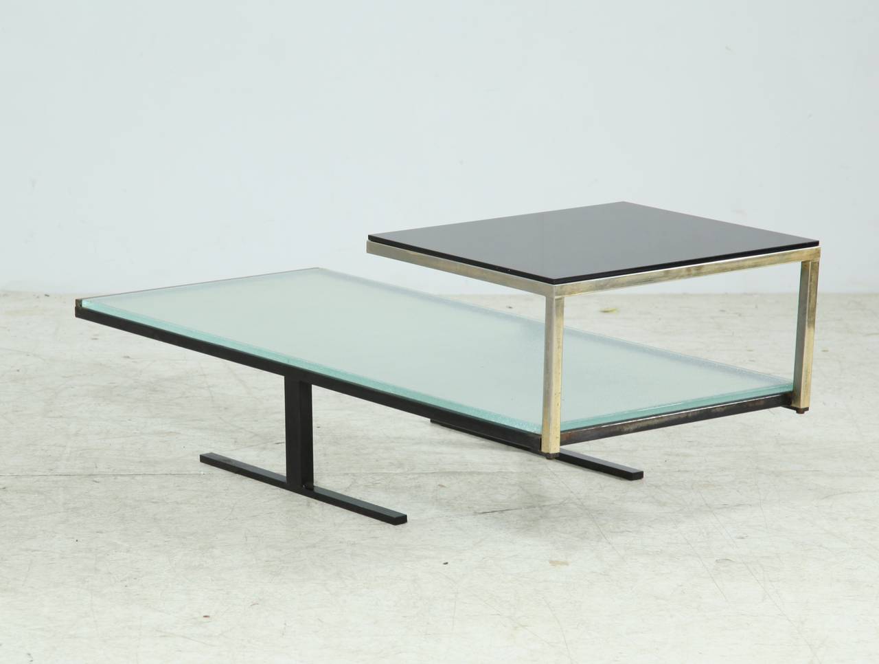 A rare and architectural coffee table in the manner of René-Jean Caillette. The table is made of a two-tiered metal frame with two removable glass tops. The first top is of clear pressed glass and the second of a dark pressed glass. A beautiful