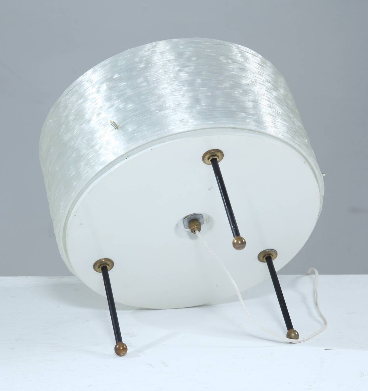 A round French table lamp on three small metal legs with brass feet, attributed to Arlus. The lamp is made of ribbed Perspex with a plexiglass diffuser on top, for a beautiful, atmospheric light distribution.
The lamp holds three light bulbs and is