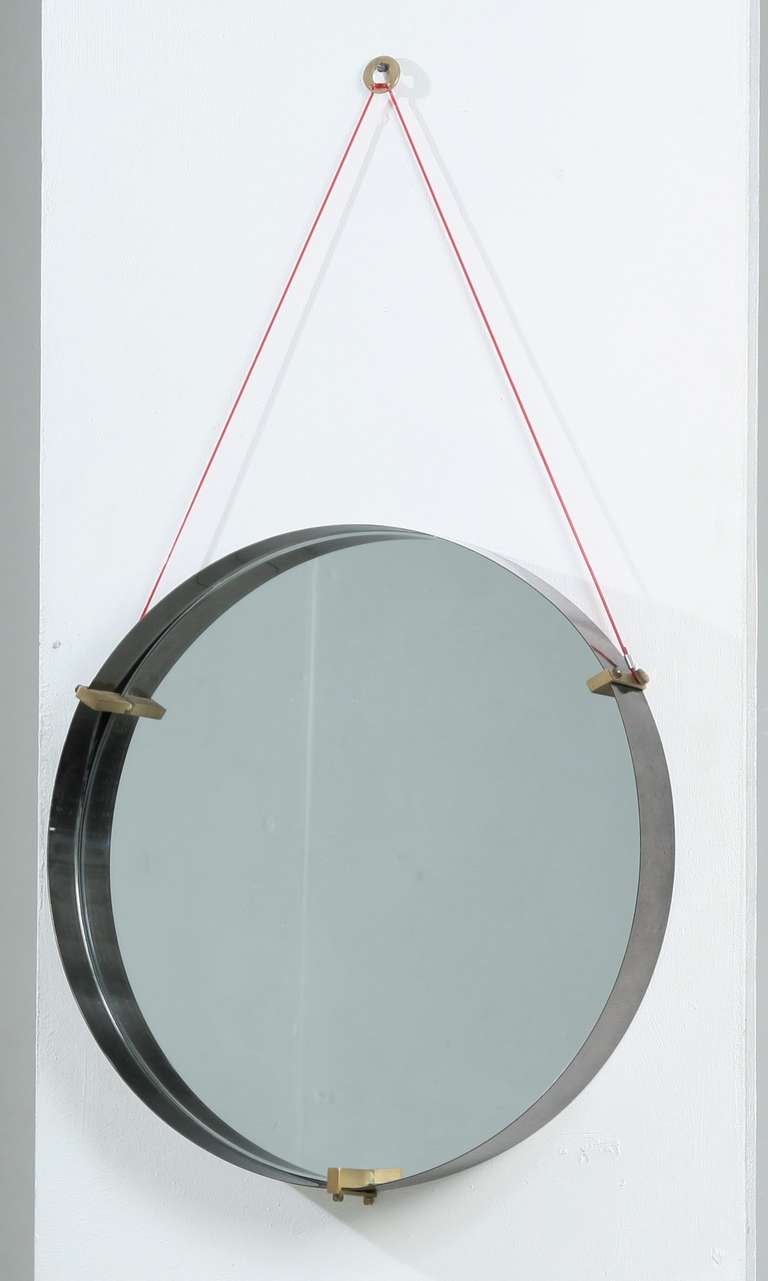 Italian minimailst round mirror, stainless steel ring with brass connecting  elements. The mirror is hung with a red thread.