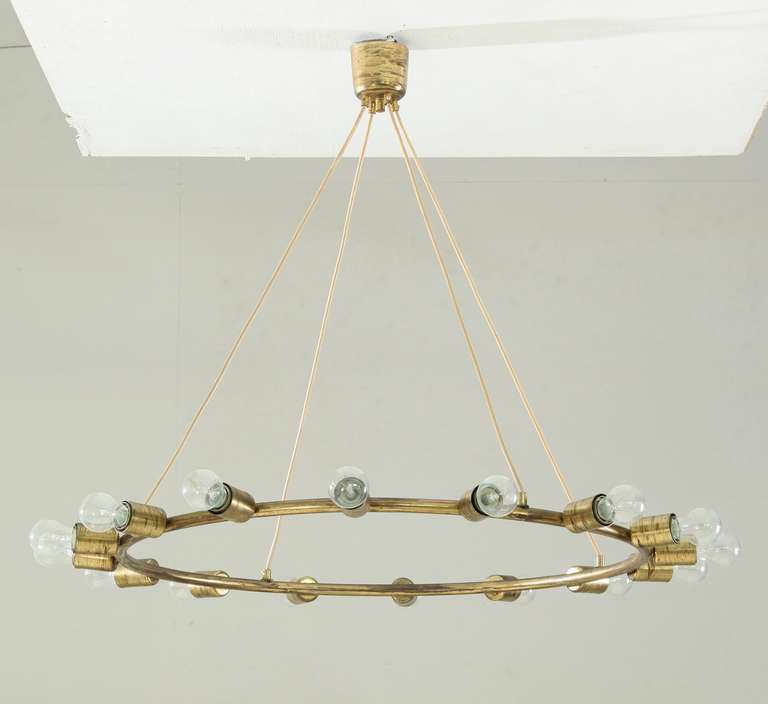 A large and minimalistic brass circular chandelier, hanging from three cords, with 16 light bulbs.