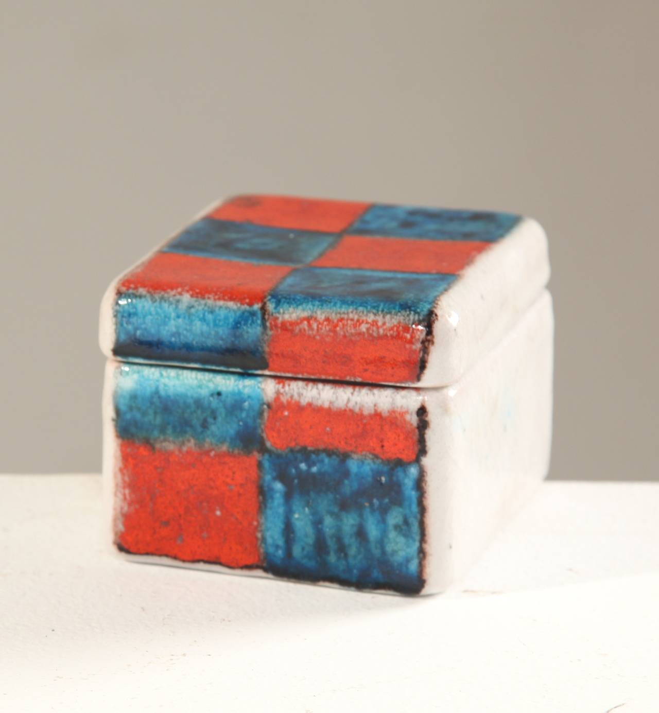 A small ceramic box with lid by Italian ceramist Guido Gambone. The box is white with an orange and blue pattern.
In a perfect condition and signed by Gambone.