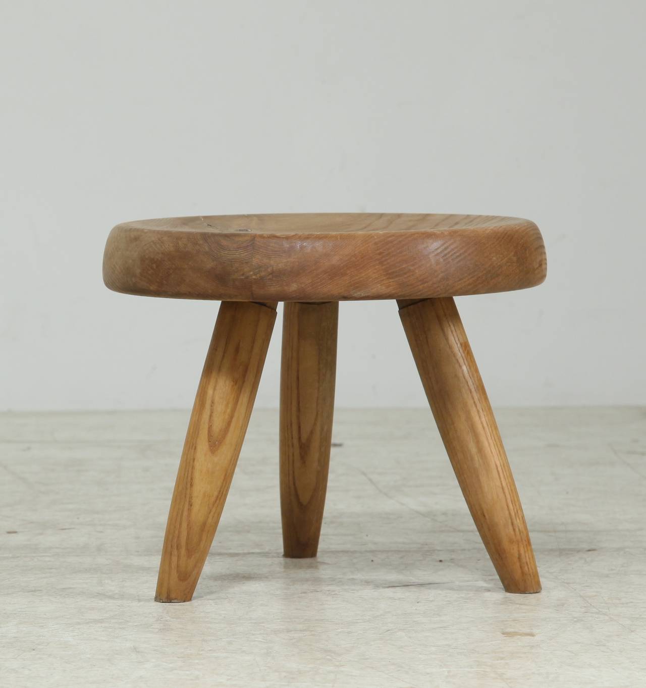 A Charlotte Perriand low tripod stool in a dark ash.