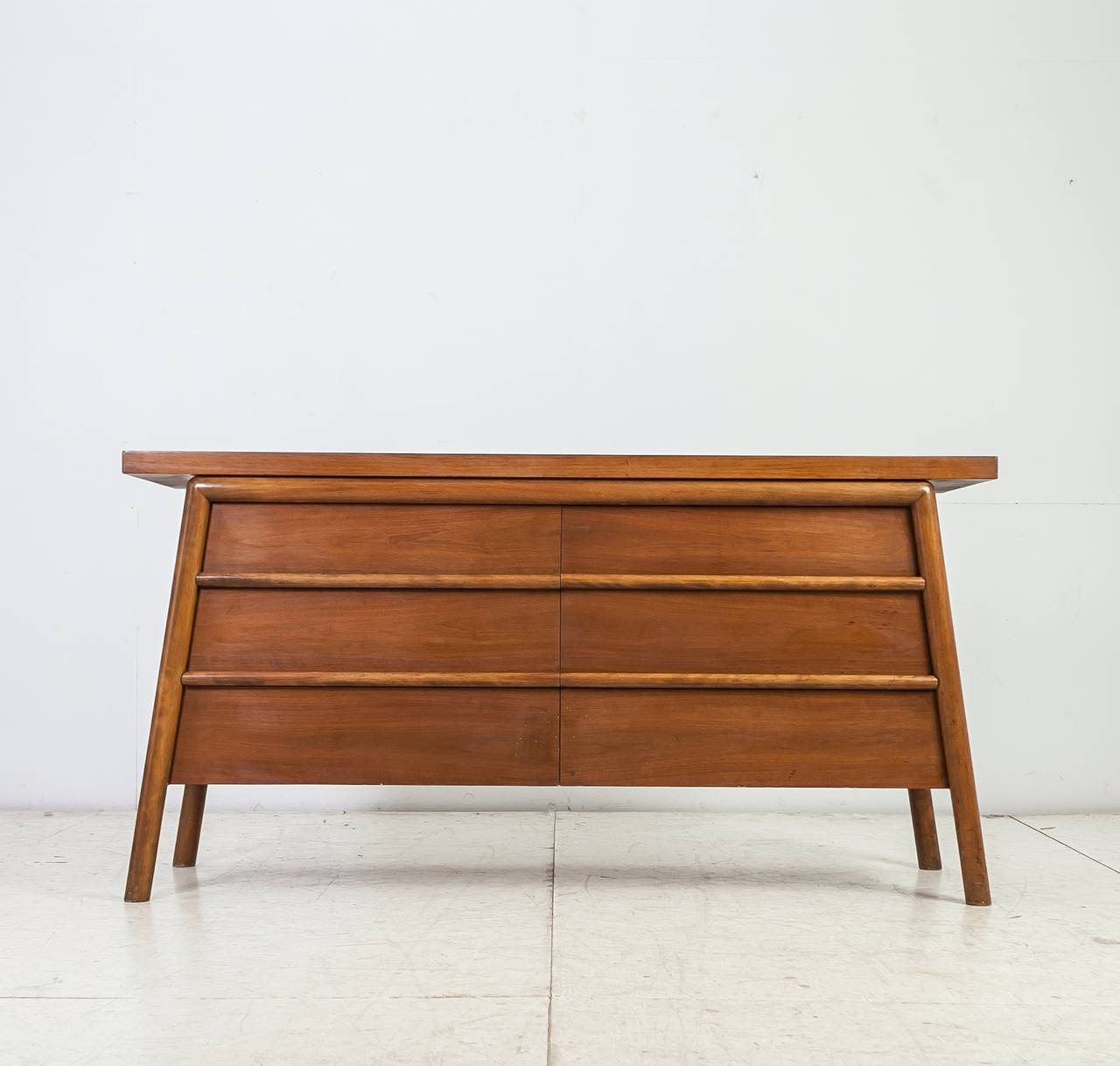 A 1950s wooden sideboard by T.H. Robsjohn-Gibbings for Widdicomb. The sideboard has six large drawers, with subtle, rounded pulls over the full length of the drawers.
This piece has a wonderful warm patina and is labeled by Widdicomb.