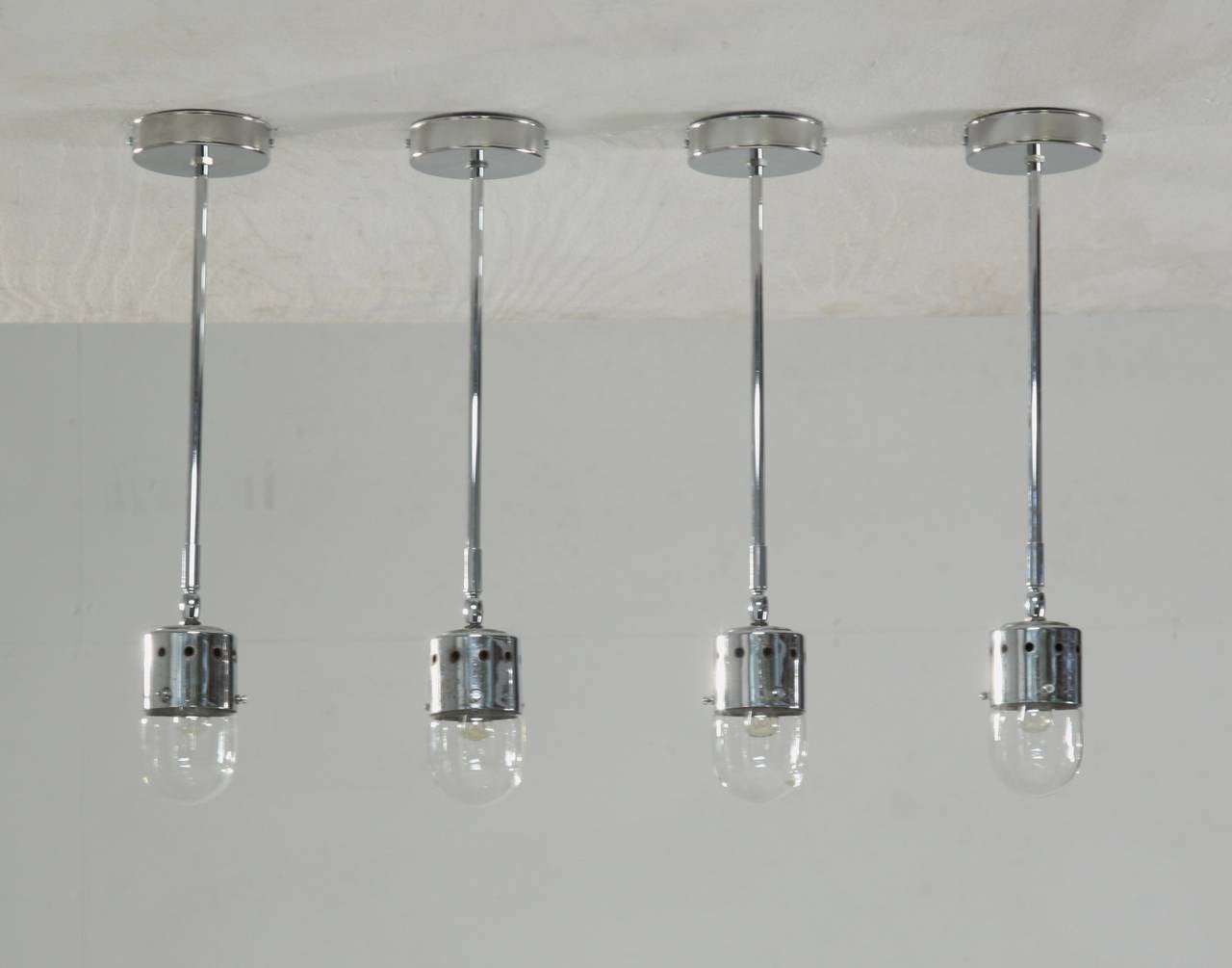 A set of four very minimalistic chrome ceiling lights from Italy. The lamps are made of a ceiling mounted stem with a perforated cylinder that holds the fitting and a bulb shaped transparant glass diffuser. The shades have a ball-joint connection,