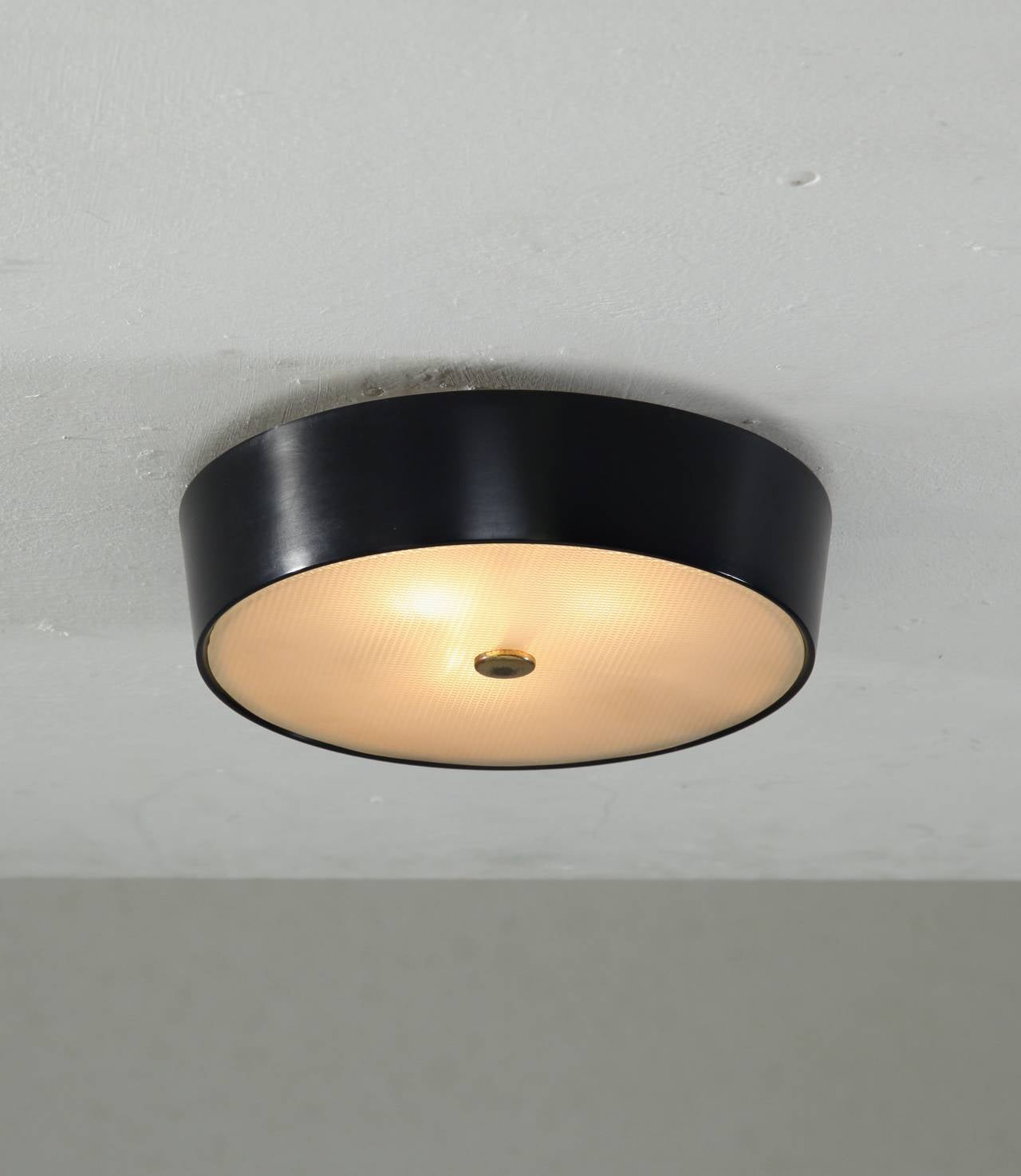 A round Stilnovo flush mount lamp made of black metal outside and white metal inside, with a textured glass diffuser.