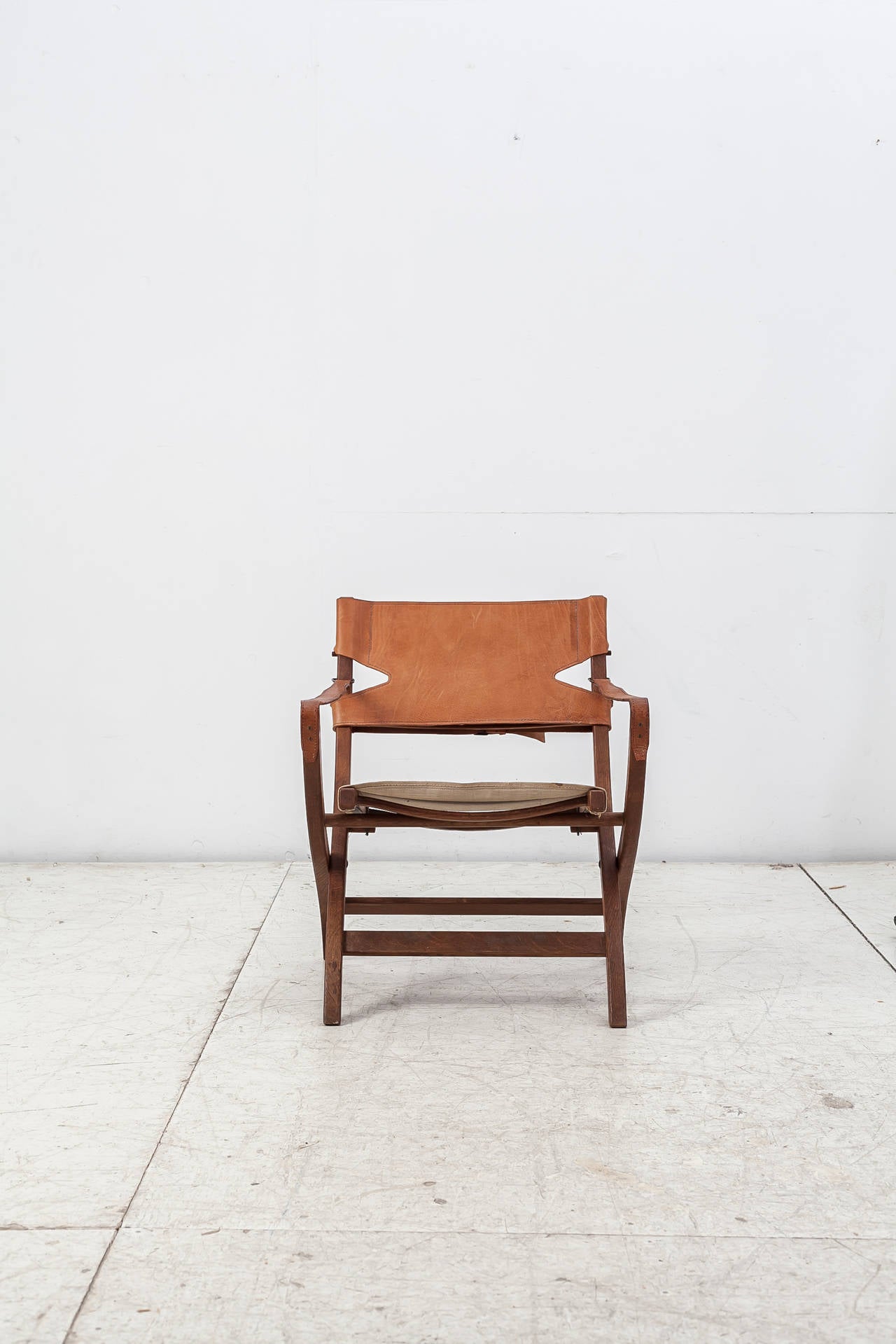 A folding safari chair by Danish designer Poul Hundevad. The chair is made of a teak frame with a canvas seating and leather back rest, with leather straps. This piece is labeled by Poul Hundevad, Vamdrup.