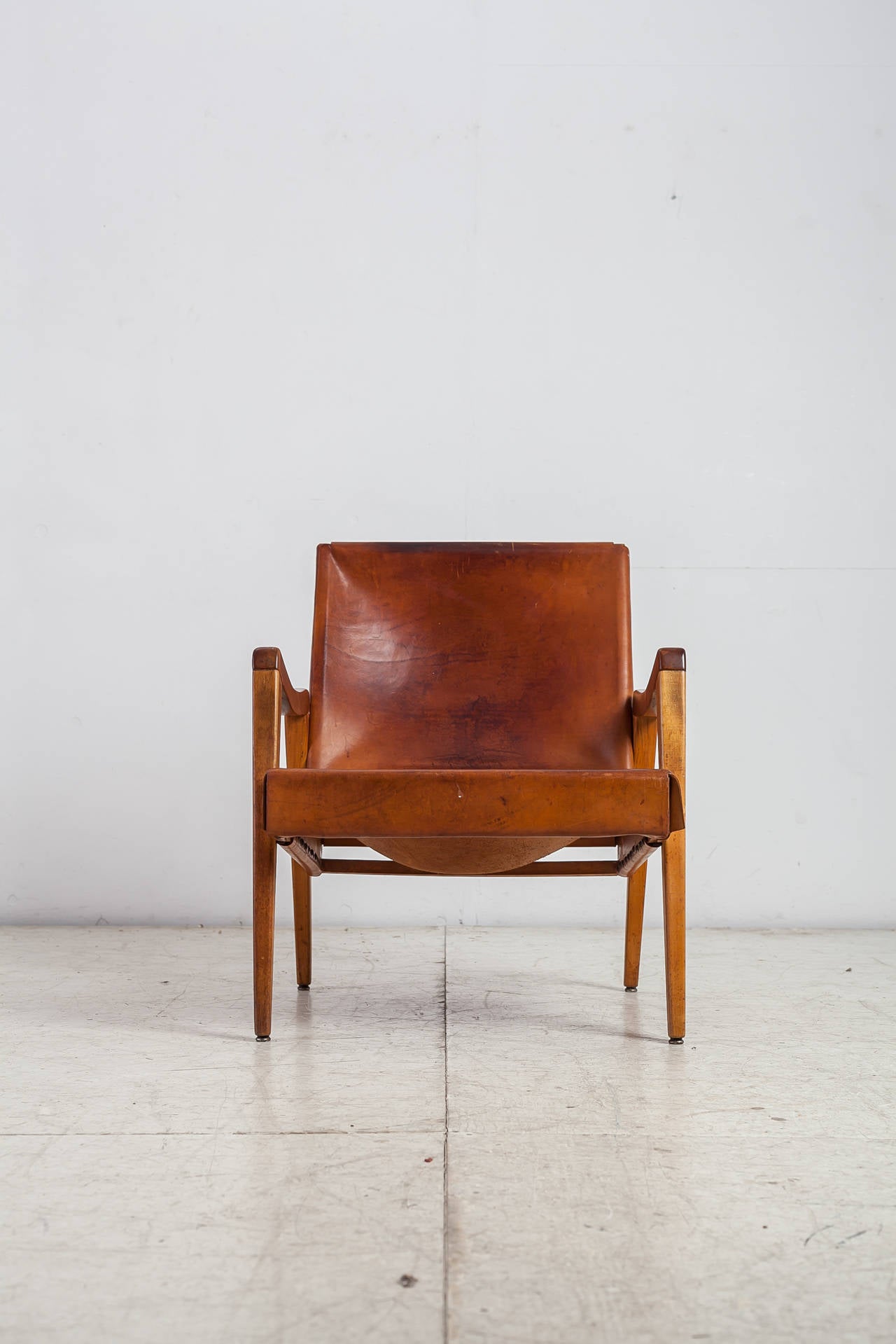 An American lounge chair made of a maple wood frame with a deep sling leather seating and backrest. The leather has a beautiful patina and the chair is in an overall good condition.