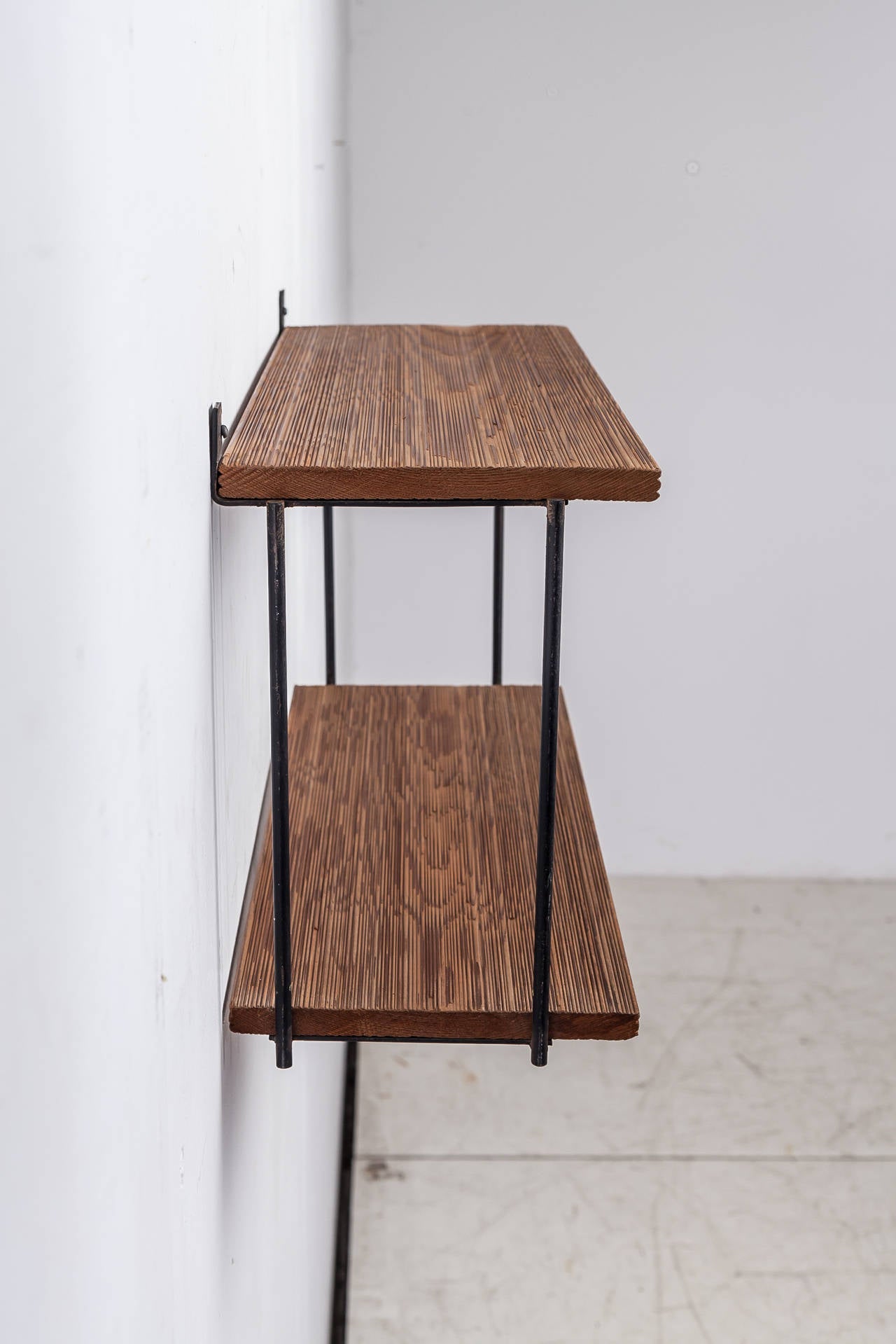 A shelving unit by Muriel Coleman, made of a black iron frame with two textured redwood shelves. The wood has a beautiful dark color and is in a wonderful condition.