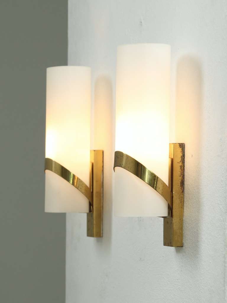 A pair of Italian brass and opaline wall lamps in the manner of Stilnovo,
The cylindrical opaline glass shades are captured in an elegant brass rim which connects to the wall mount.