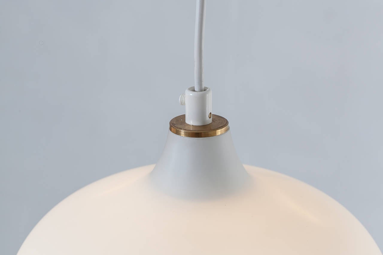 A pair of Tapio Wirkkala model 51129 pendant lamps made of opaline glass with a brass ceiling-mount. Wirkkala designed the lamps in 1958 for Idman.