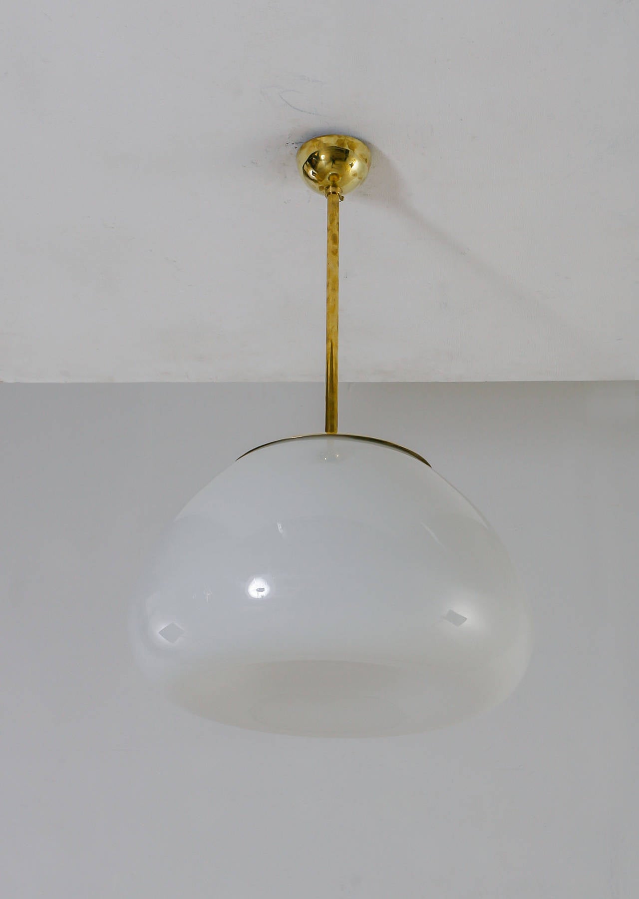 A very large and rare model '50106' opaline glass pendant with a brass cap, by Gunnel Nyman for Idman. The opaline glass diffuser, which curves inwards, is connected to the ceiling with a brass stem. It has three light bulbs.
The lamp is marked by