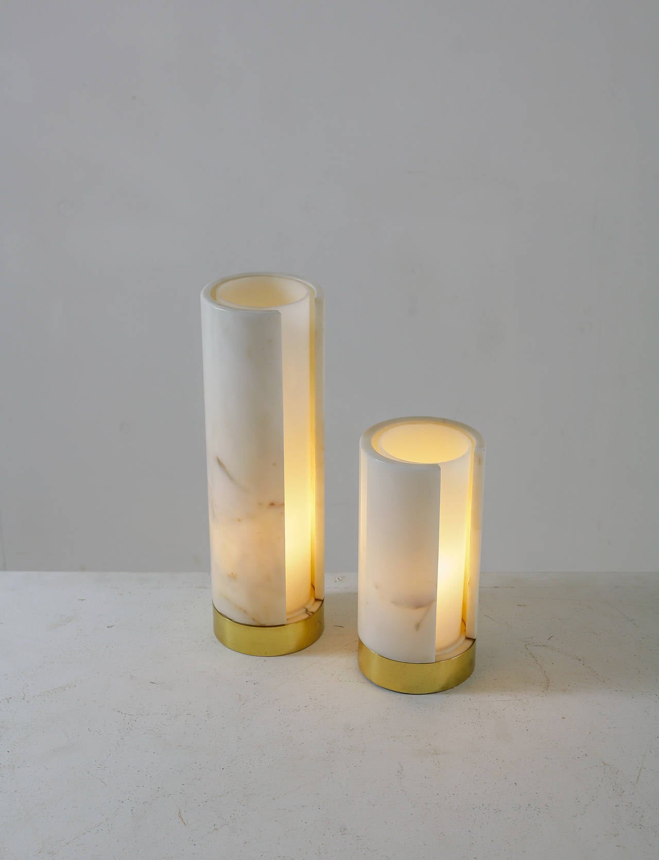 A pair of cylindrical table lamps made of a marble shade with a plexiglass diffuser inside, standing on a brass base. The marble has a very light pattern and is in excellent condition. 

The small one has a diameter of 13.5 cm and is 28 cm high.