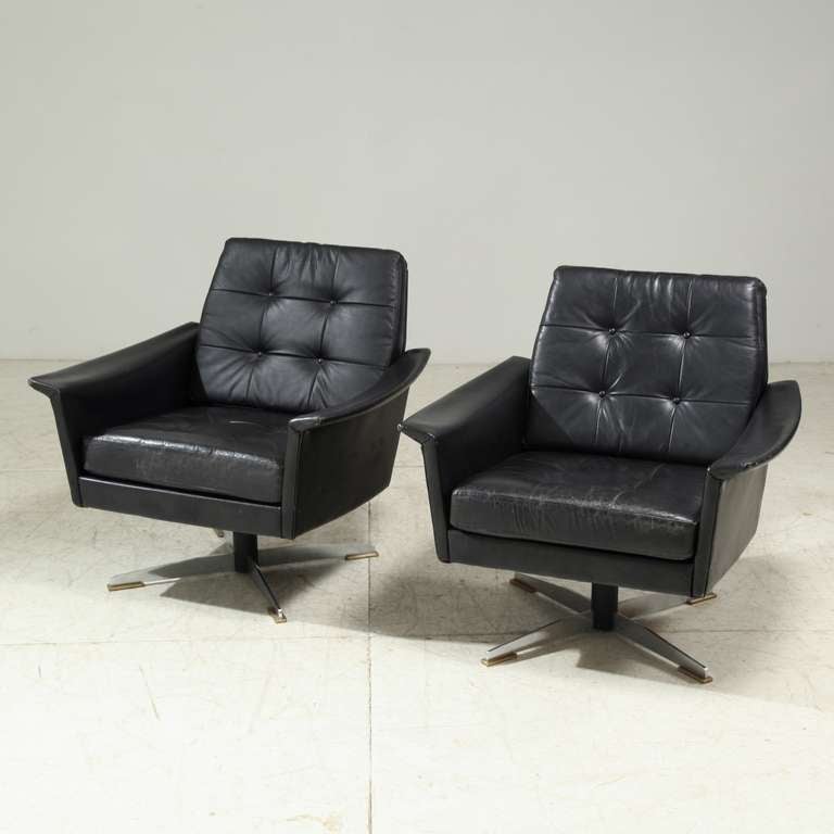 Two black club chairs in black leather on a metal swivel base. They are reminiscent of the chairs of Horst Brüning.