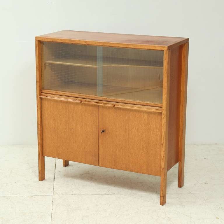 An oak cupboard or bar with two doors and two sliding glass panels, with a draw-leaf. Designed by Cees Braakman for Pastoe, late 1940s, early 1950s. Marked by Pastoe at the back.