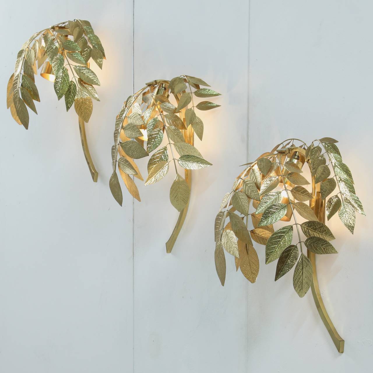 A set of three wall appliques that appear like brass coated tree branches with leaves.
The E27 light bulb is covered enough not to show and free enough to distribute the light through the leaves.