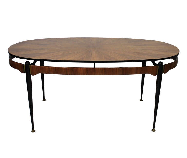 An Italian 'd' end dining table of exceptional quality by Ico Pariri, Milan. Comprising a black enamelled frame with brass detail with a moulded oak and walnut frieze and marquetry top with a star burst design.