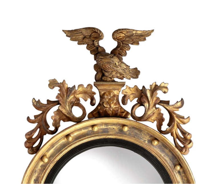 A lovely 19th Century circular gilded convex mirror with ebonised slip, surmounted with a cresting carved eagle with a carved foliate apron.
