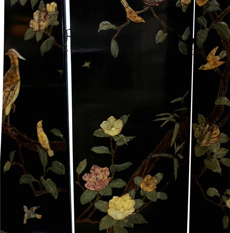 A beautiful Chinese Quing Dynasty Black lacquered coromandel four fold screen, depicting humming birds, parrots, finches and lotus flowers all out of hand carved jade and other stones. The reverse side has a modest design in gold leaf.