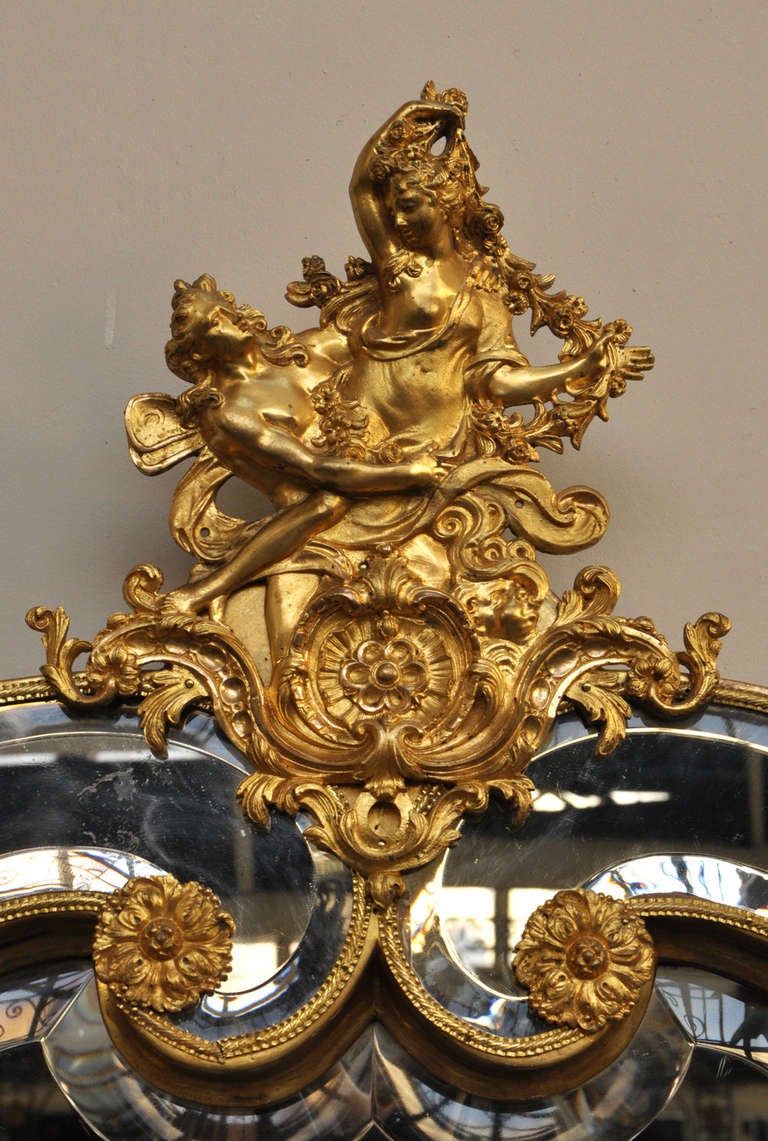 This exceptional antique mirror was realized in gilded bronze in the 19th century. Napoleon III style, the upper part of the mirror is decorated with two dancing women. The beveled mirrors are the original ones.  The realization of this mirror is
