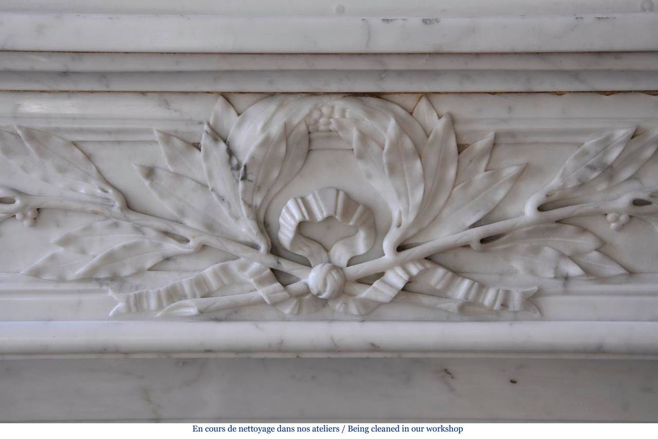 This antique Louis XVI style fireplace was made out of Carrara marble during the 19th century. The curved frieze is sculpted with laurel branches. 
The fireplace comes with its original cast iron insert.