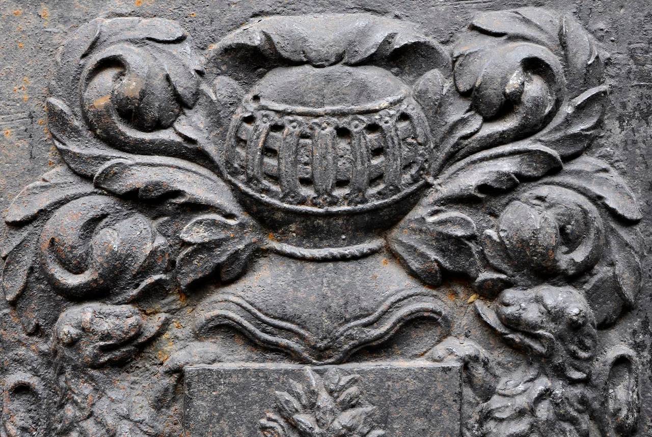 This antique 18th century cast iron fireback is ornated with a knight helmet, two lions and a coat of arms with a branch of laurels. Large dimensions.