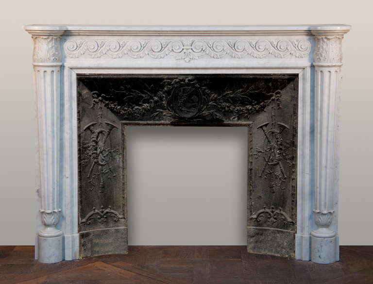 Sculpted in a top quality Carrara marble. Fluted half columns crowned by acanthus leaves capitals figures the jambs of this fireplace. The frieze is delicately carved with waves and foliages. 
This fireplace is sold with an antique cast iron insert.