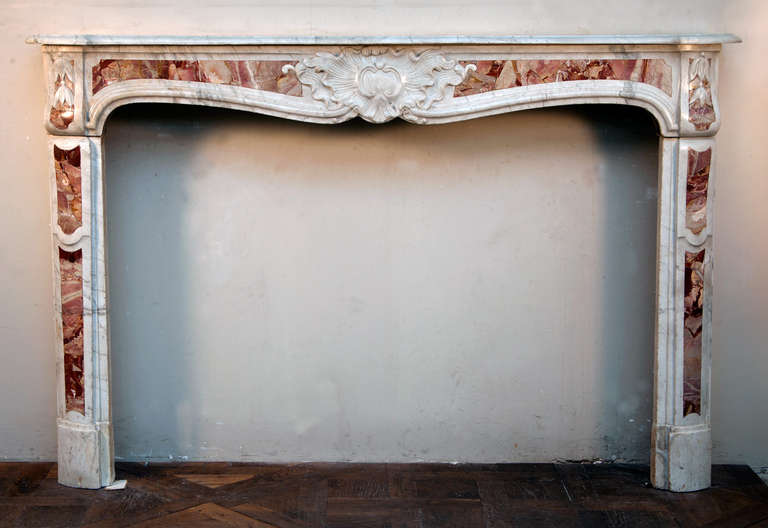 This antique Louis XV period fireplace was made out of Carrara marble with Sarrancolin marble cabochons in the 18th century. Coming from the Provence area, in the South of France, this fireplace is slightly curved. The center of the frieze is