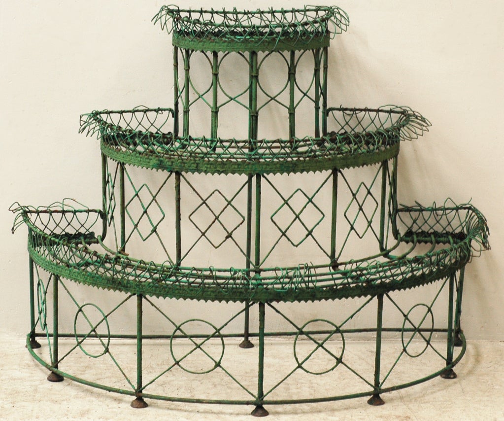 This iron plant stand was realized in the 19th century. It has three tiers and a half-moon shape.