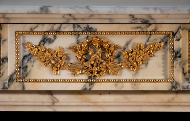 This antique Louis XVI style fireplace was made out of Panazeau marble, a marble coming from the area of Carrara in Italy. The fireplace is 19th century period.  All sculptures are made of gilded bronze. Both jambs are made as half columns, ornated