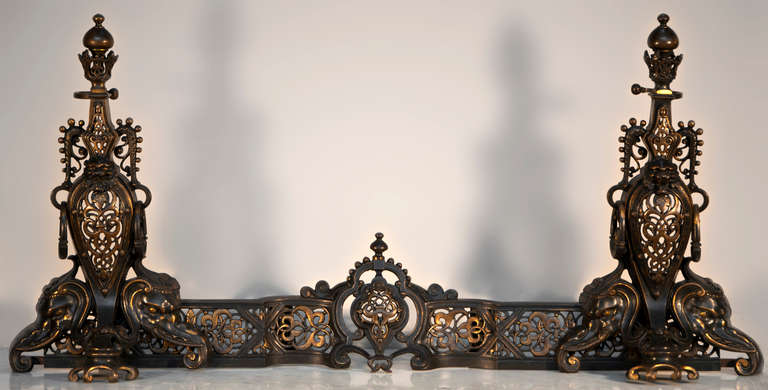Made out of bronze with gilded and brown patinas, this fire fender is highly ornated. The openwork decoration is made of interlacing with floral elements. Both andirons are supported by powerful elephants heads.