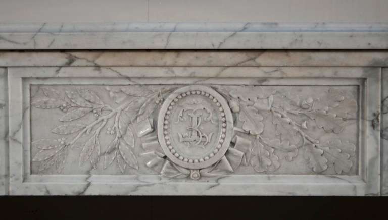 This rare antique Louis XVI period fireplace was made out of white veined marble during the 18th century. The frieze is composed of three panels. The center one is carved in low relief with the monogram 