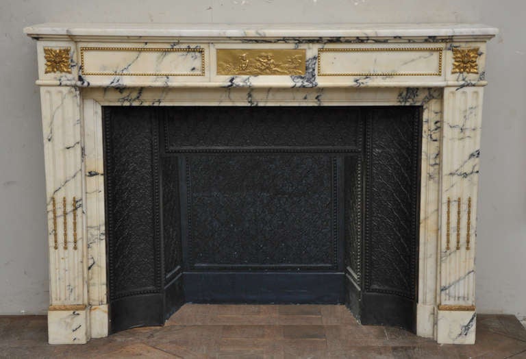 This antique Louis XVI style fireplace was realized in the 19th century in a Panazeau marble, from Italy. This fireplace is ornated with bronze. The center of the frieze is decorated with a low-relief bronze with putti. 
This fireplace is sold with