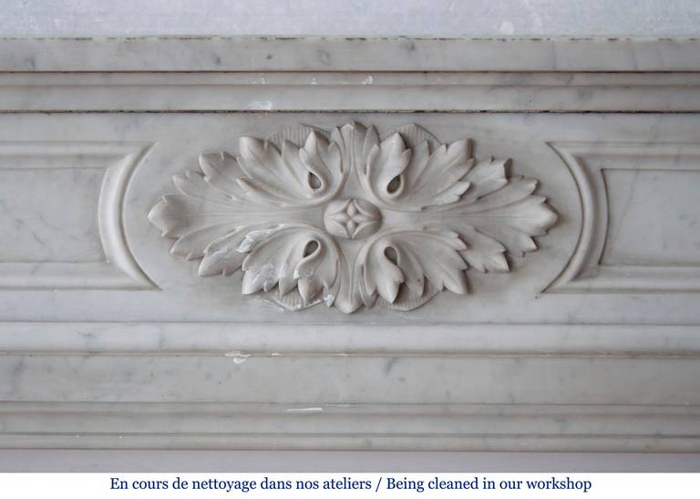 19th century Louis XVI style fireplace with round corners was made out of Carrara marble during the 19th century. Ornated with an acanthus leaf medallion, the fireplace features fluted legs with asparagus leaves decor. 
The fireplace is sold with
